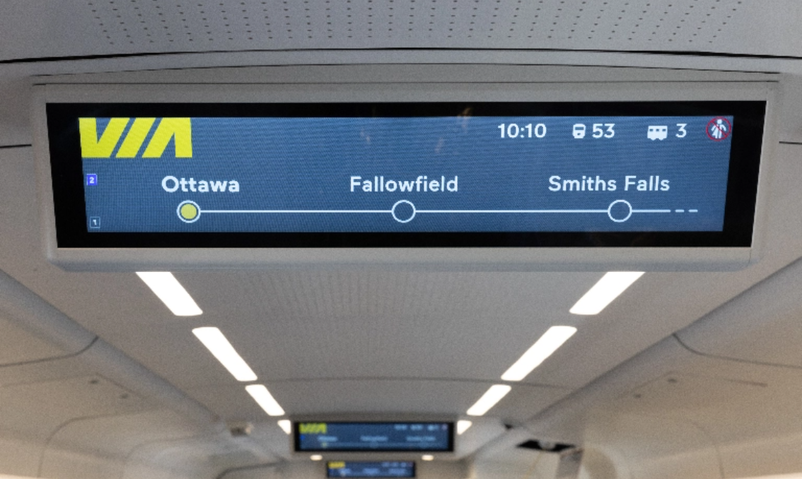 Picture of an on-board announcement screen on the ceiling of a train car. Other announcement screens can be seen in the background. 