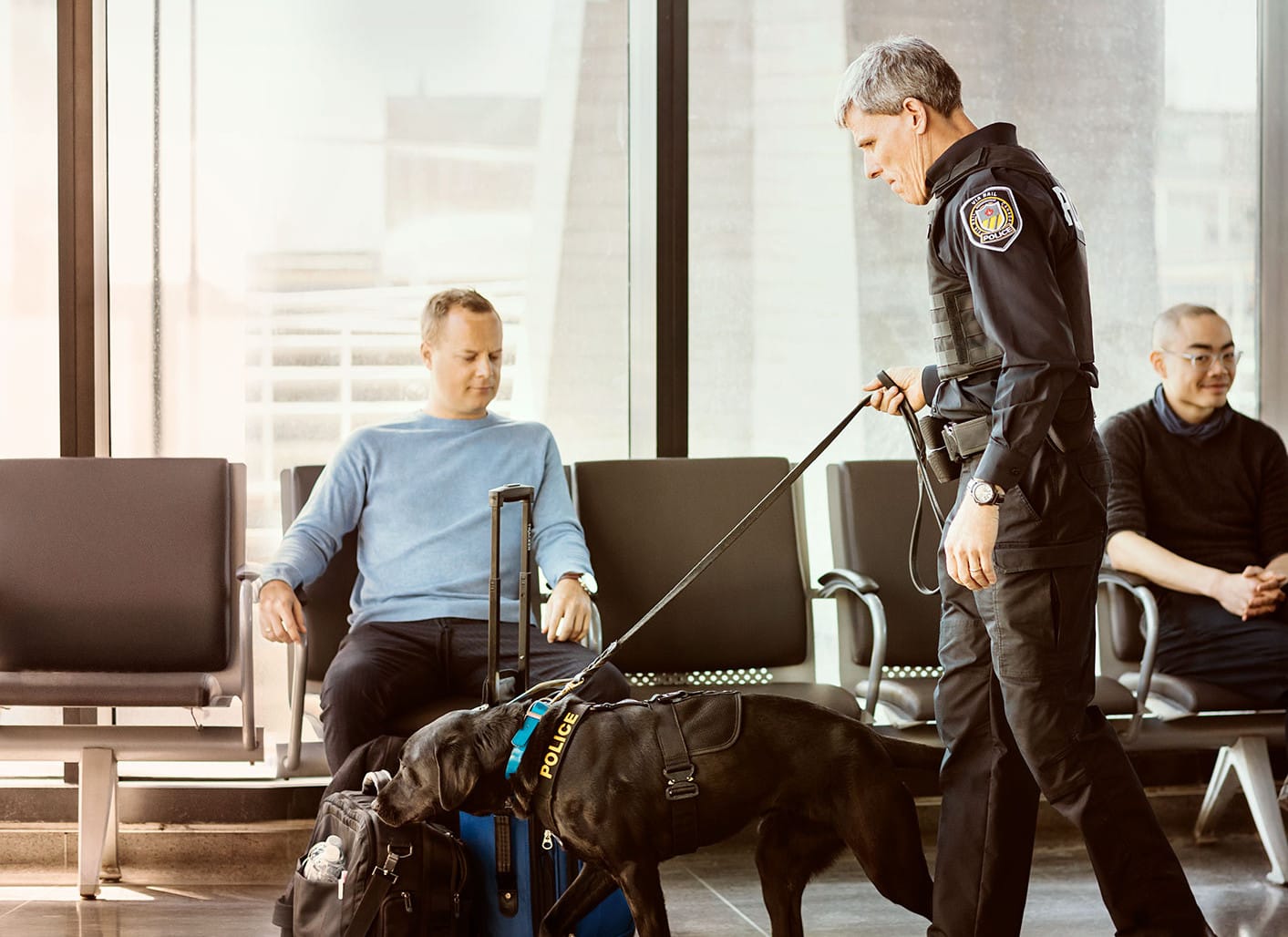 Photo d'un policier avec un chien qui sent les valises d'un voyageur.